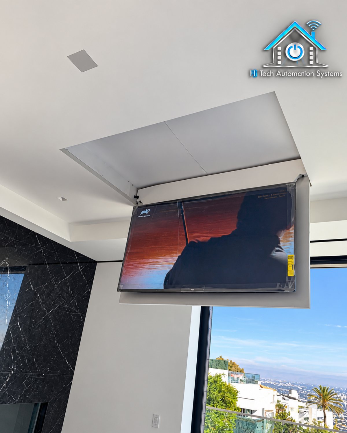 Motorized television lowering from the ceiling in a room with floor-to-ceiling glass and a hillside view.