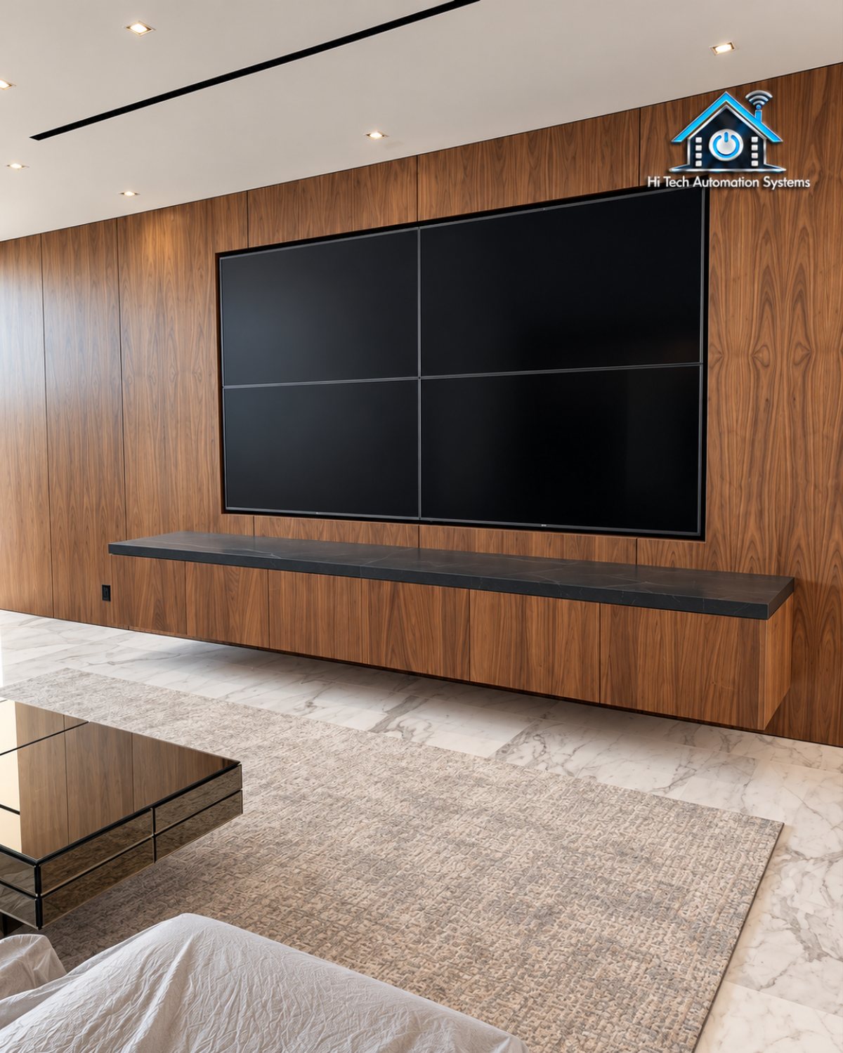 Living room with a large television on a wood-panelled feature wall above a floating shelf, marble floor and natural light.